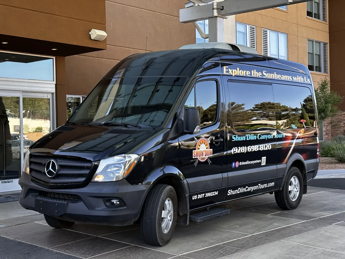 The black Shun'Diin Mercedes Sprinter parked at a Page hotel entrance for pickup
